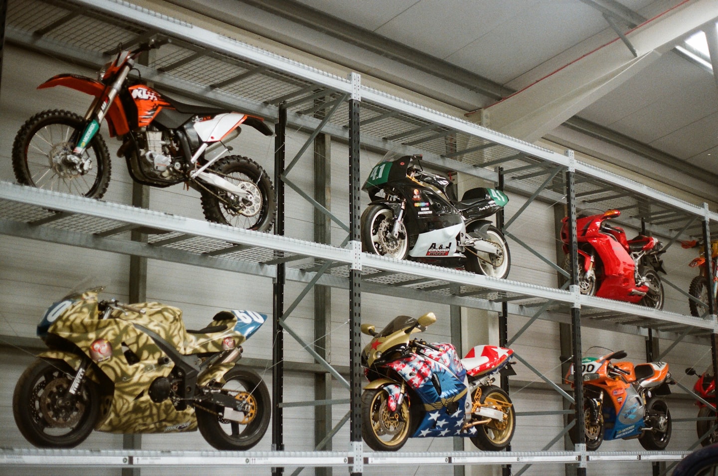 Various motorcycles parked on metal storage racks in a warehouse.