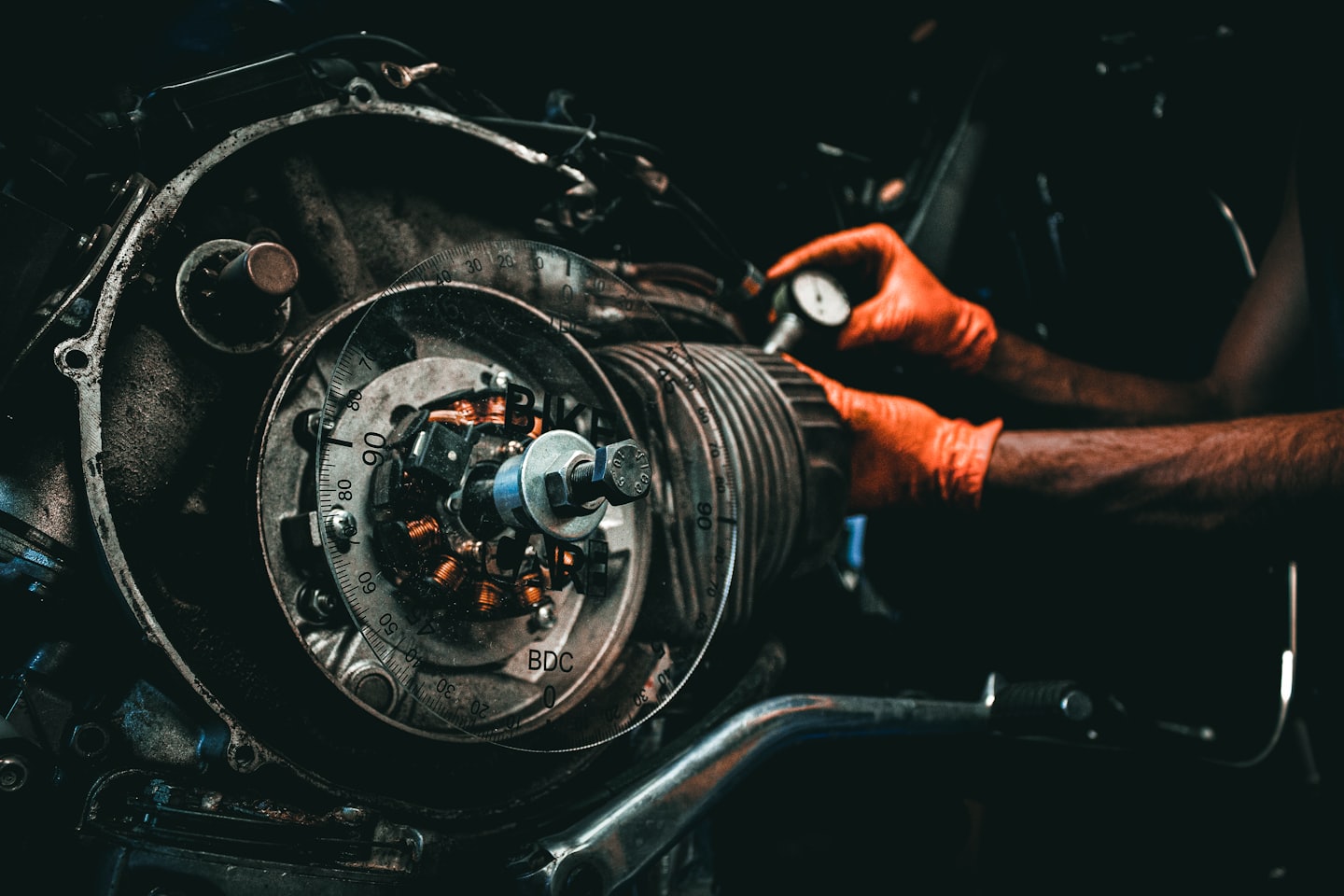 Mechanic's gloved hands working on a motorcycle engine.